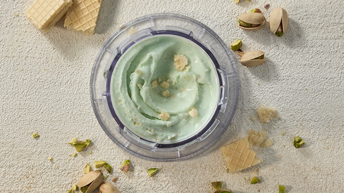 Green ice cream in container with cookie pieces and pistachios nearby.